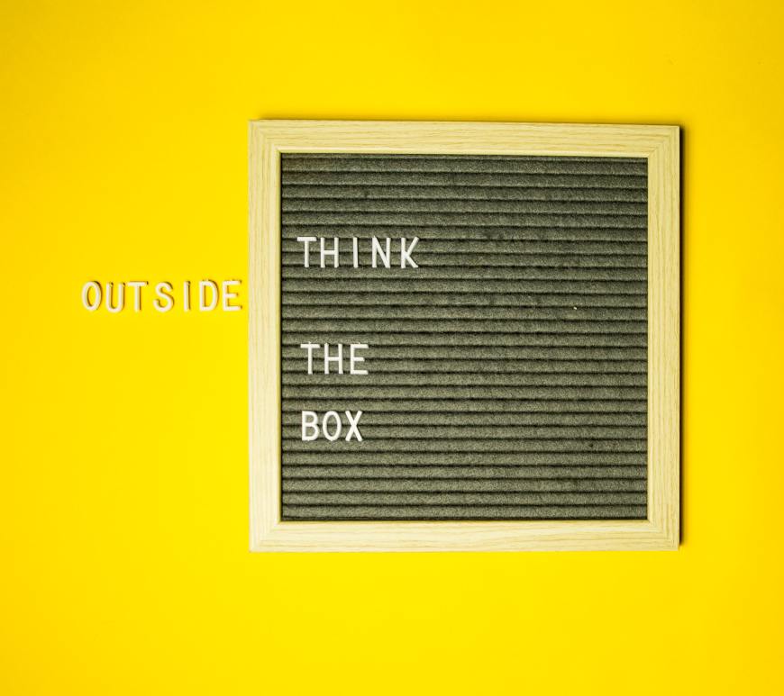 board with the words "think" "the" and "box" with the word "outside" outside the box all on a yellow background