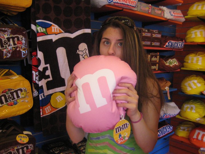 renata looking at the camera while pretending to eat a giant m&m pink pillow surrounded by chocolate merchandise