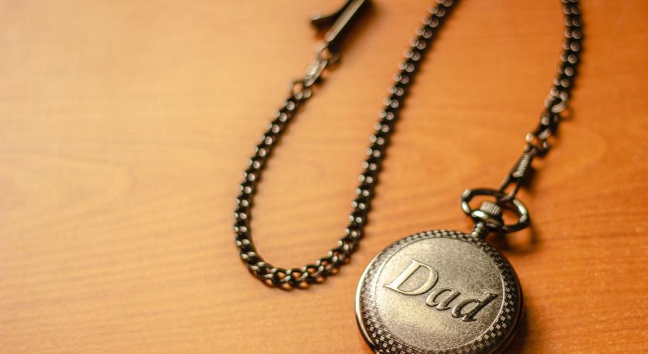 gold pocket watch with "Dad" written on it laying on a wooden surface