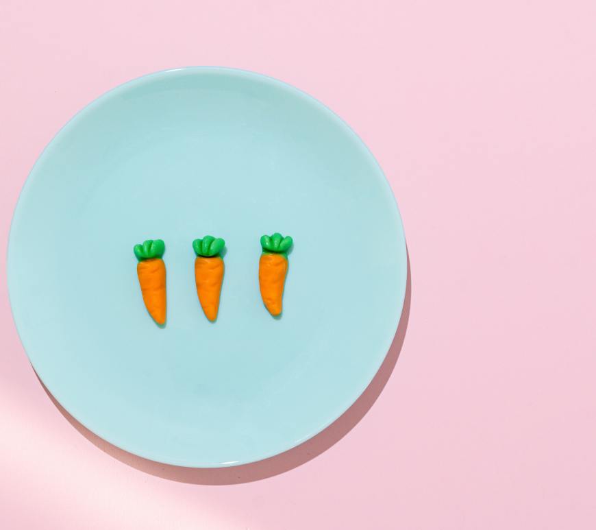 three artificial carrots on a blue plate all on a pink background