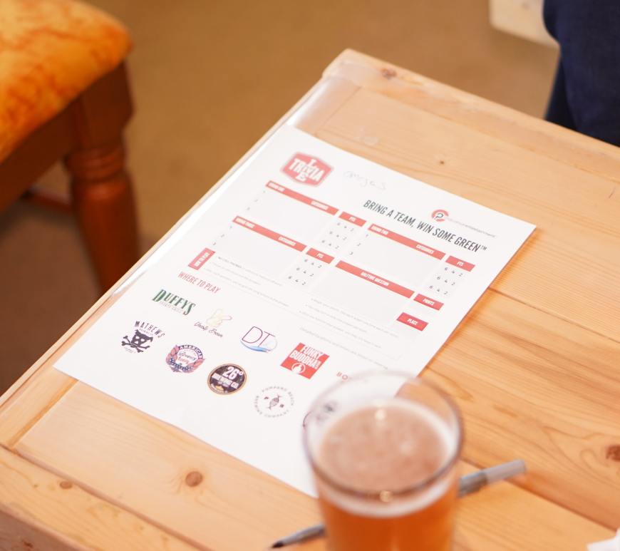trivia paper, beer, and pen on a wooden table
